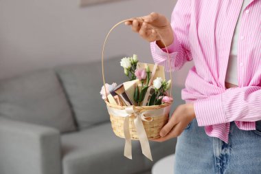 Elinde kozmetik ürünler, hediye kutuları ve çiçeklerle dolu sepeti olan genç bir kadın.