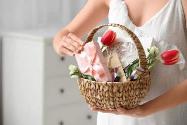 Kozmetik ürünleri, hediye kutusu, çikolata ve çiçeklerle dolu sepeti elinde tutan genç bir kadın.