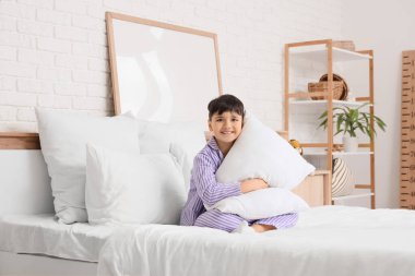 Çizgili pijamalı, yastıklı tatlı çocuk evde yatakta oturuyor.