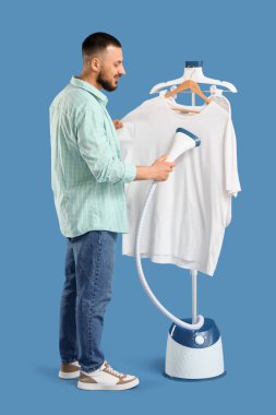 Genç adam mavi arka planda beyaz tişört giyiyor.