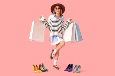 Pembe arka planda yüksek topuklu ayakkabı ve bahar kıyafetleri içinde şık genç bir kadın.