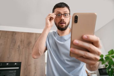 Mutfakta cep telefonu kullanan gözlüklü genç adam şok oldu.