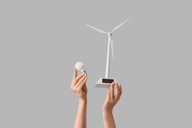 Rüzgâr türbini modelli kadın eller ve arka planda ampul. Ekoloji kavramı