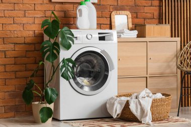 Tuğla duvarın yanında modern çamaşır makinesi olan çamaşır odasının içinde.