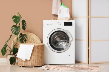 Çamaşır odasının içi. Kahverengi duvarın yanında modern çamaşır makinesi var.