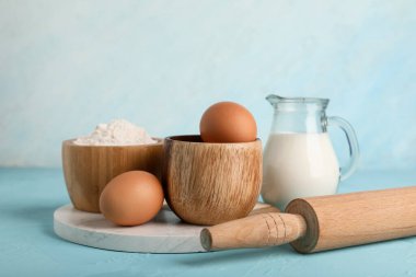 Taze tavuk yumurtası, un, bir sürahi süt ve renk arka planında oklavalar.