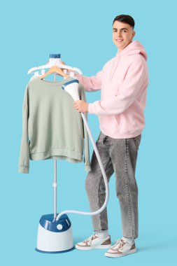 Genç adam mavi arka planda buharlı giysiler giyiyor.