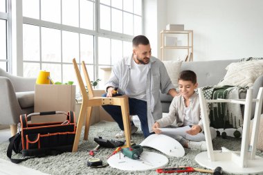 Baba ve oğlu talimatlarla evde mobilya monte ediyorlar.