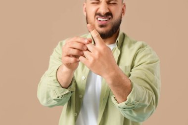 Bej arka planda bantlanmış parmağı olan genç adam, yakın plan.