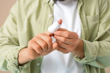Bej arka planda bandajlı parmağı olan genç adam, yakın plan.