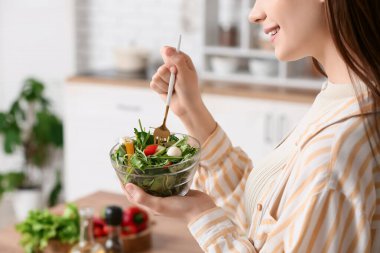 Genç bir kadın mutfakta taze sebze salatası yiyor.