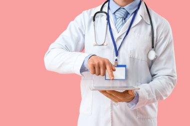 Pembe arka planda tablet bilgisayarla çalışan erkek doktor, yakın plan.