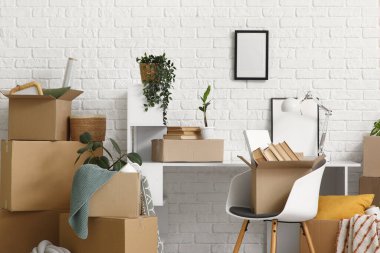 Taşındığı gün beyaz tuğla duvarın yanındaki karton kutularla dolu çalışma yerinde.