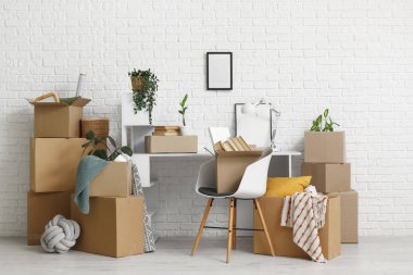 Taşındığı gün beyaz tuğla duvarın yanındaki karton kutularla dolu çalışma yerinde.