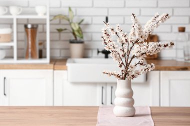 Mutfaktaki ahşap masada güzel dalları olan bir vazo.