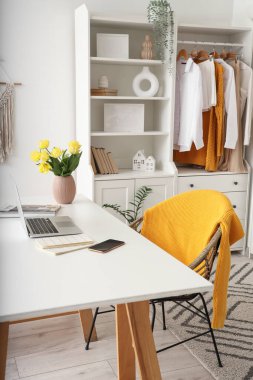 Ev ofisindeki masada bahar çiçekleri olan dizüstü bilgisayar ve vazo.