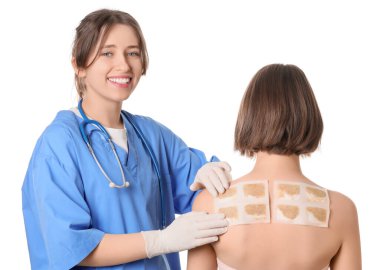 Kadın doktor hastanın sırtına hardal yapıştırıcı sürüyor.