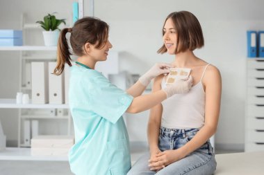 Kadın doktor klinikte hastanın göğsüne hardal yapıştırıyor.