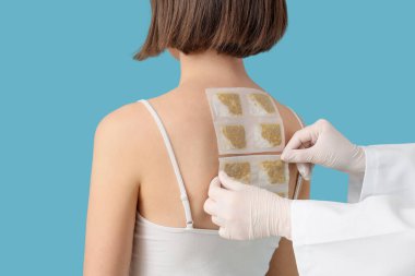 Kadın doktor hastanın sırtına hardal yapıştırıyor. Mavi arka plan, yakın plan.