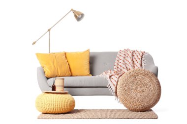 Beyaz arka planda puf ve lamba olan gri kanepe.