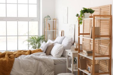 Katlanan ekran, raf üniteleri ve bitkilerle aydınlık yatak odasının içi