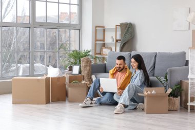 Taşınırken odada dizüstü bilgisayar kullanan mutlu genç çift.