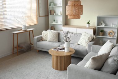 Oturma odasının içinde kanepe, raflar ve sehpanın üstündeki vazolarda çiçek açan dallar.