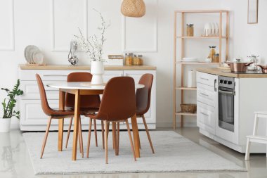 Mutfağın içinde tezgahlar, raflar ve yemek masasındaki vazolarda çiçek açan dallar var.