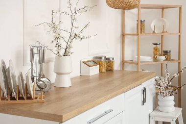 Mutfağın içinde raflama ünitesi ve tezgahtaki vazolarda çiçek açan dallar.