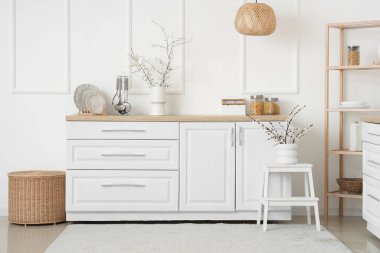 Mutfağın içinde raflama ünitesi ve tezgahtaki vazolarda çiçek açan dallar.