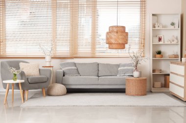 Oturma odasının içinde kanepe, koltuk, raf ünitesi ve masaların üzerindeki vazolarda açan dallar.