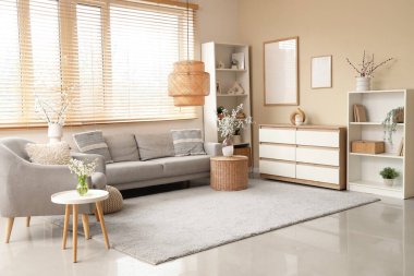 Oturma odasının içinde kanepe, koltuk, raflar ve masaların üzerindeki vazolarda açan dallar.