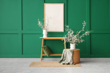 Oturma odasındaki yeşil duvarın yakınındaki masalarda çiçek açan vazolar.