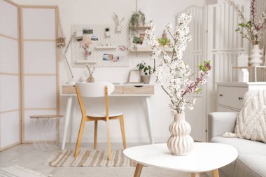 Işık ofisindeki masanın üzerinde çiçek açan dalları olan vazo.