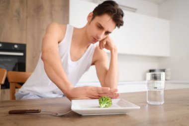 İştahsızlığı olan genç adam mutfakta yemek yemeyi reddediyor.