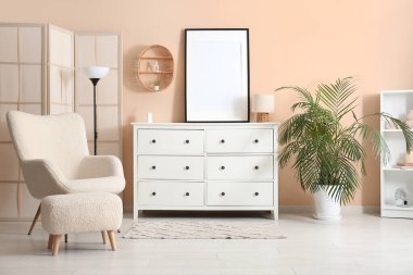 Boş fotoğraf çerçevesi ve rahat koltuğu olan beyaz çekmeceler.