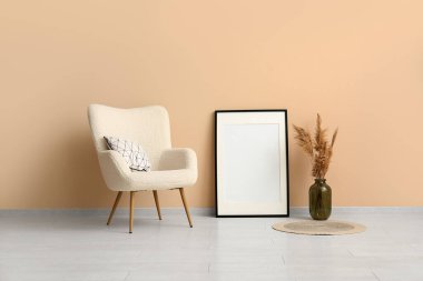 Yumuşak yastıklı rahat koltuk ve odada bej duvarın yanında boş fotoğraf çerçevesi.