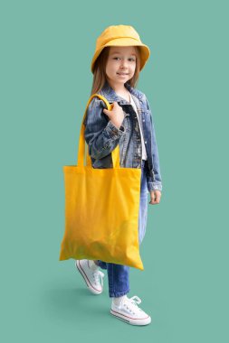 Yeşil arka planda tekstil çantası olan, kova şapkalı şirin bir kız.