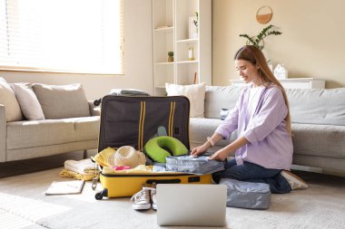 Evde dizüstü bilgisayarı olan bir turist valizini hazırlıyor.