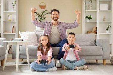 Mutlu baba ve küçük çocukları evde video oyunu oynuyorlar.