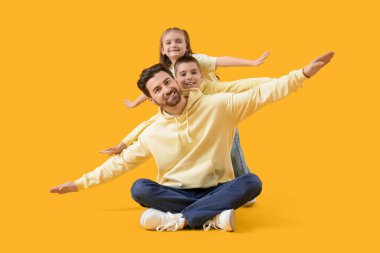 Sarı arka planda küçük çocukları olan mutlu bir baba.