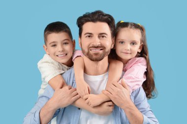 Küçük çocukları mavi arka planda sarılırken mutlu bir baba.