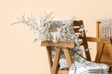 Bej duvarın yakınındaki tahta sandalyede çiçek açan dallar.