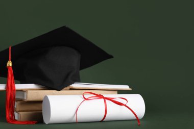 Mezuniyet şapkası, kitaplar ve yeşil arka plan diploması.