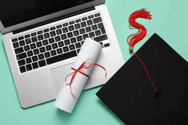 Mezuniyet şapkası, dizüstü bilgisayar ve turkuaz arka plan diploması. Çevrimiçi eğitim kavramı