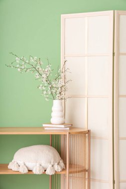 Katlanan ekran ve çiçek açan ağaç dalları yeşil duvarın yanındaki ahşap masada.