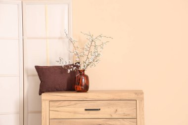 Katlanan ekran ve çiçek açan ağaç dalları bej duvarın yanındaki şifoniyerde.