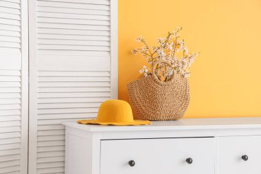 Katlanan ekran ve çiçek açan ağaç dalları turuncu duvarın yanındaki şifoniyerde.