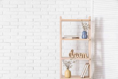 Beyaz tuğla duvarın yanındaki raf ünitesinde katlanır ekran ve çiçek açan ağaç dalları