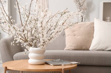 Oturma odasının iç tarafındaki masada çiçek açan dalları ve dergileri olan vazo, yakın plan.